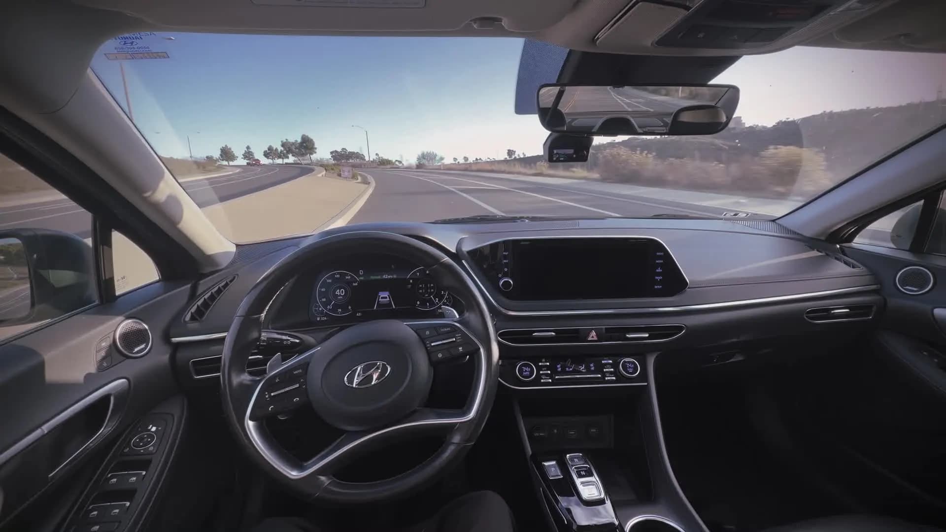 View from the driver's seat of a car on a highway with a comma four mounted below the rearview mirror